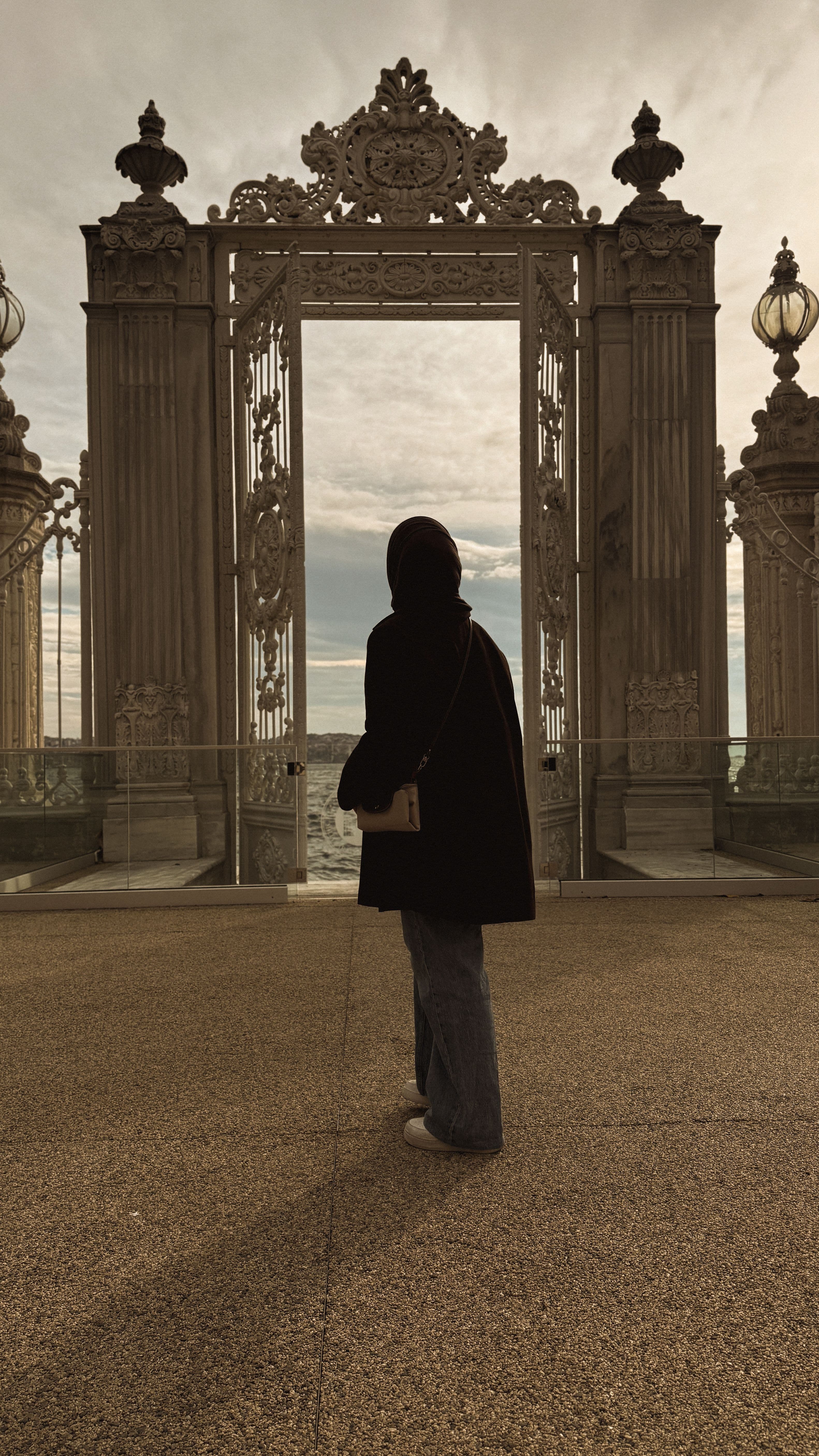 Person standing in an ornate carved stone gateway by the water